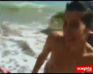 भव्य किशोर समुद्र तट पर अपना नग्न शरीर दिखा रहा है।